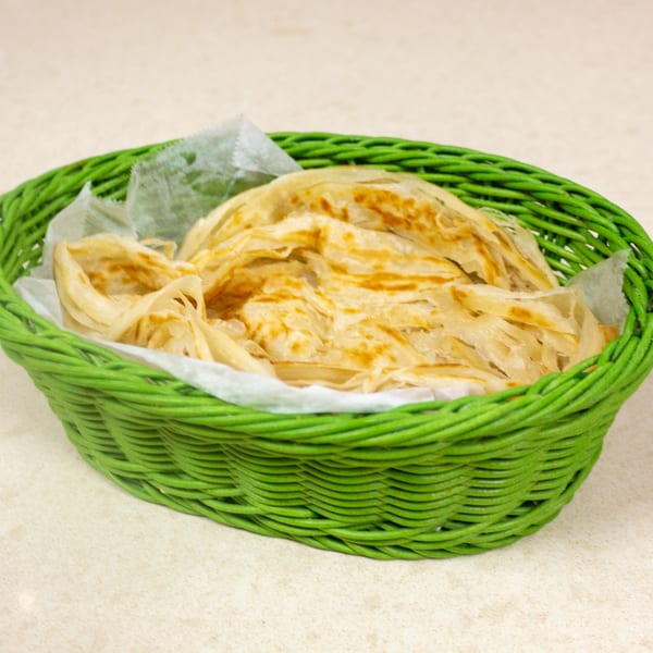 Flaky, golden-brown paratha bread served in a vibrant green woven basket lined with white paper.