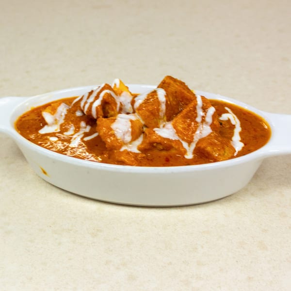 A white oval dish filled with orange curry, topped with white cream drizzle.