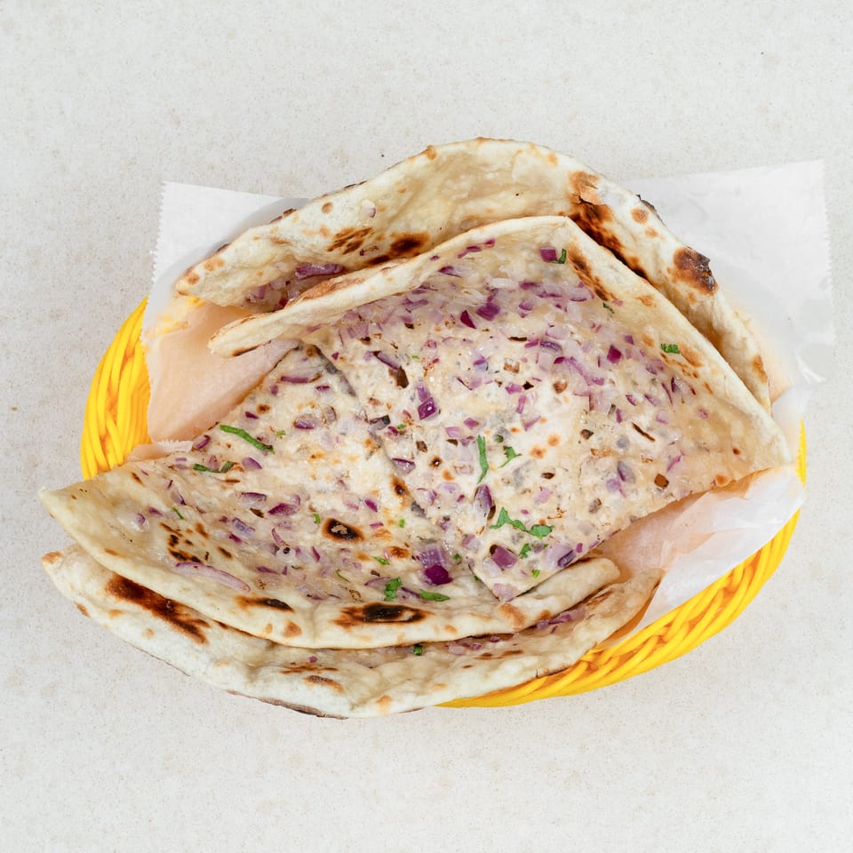 A yellow basket filled with onion naan bread, garnished with red onions and cilantro.