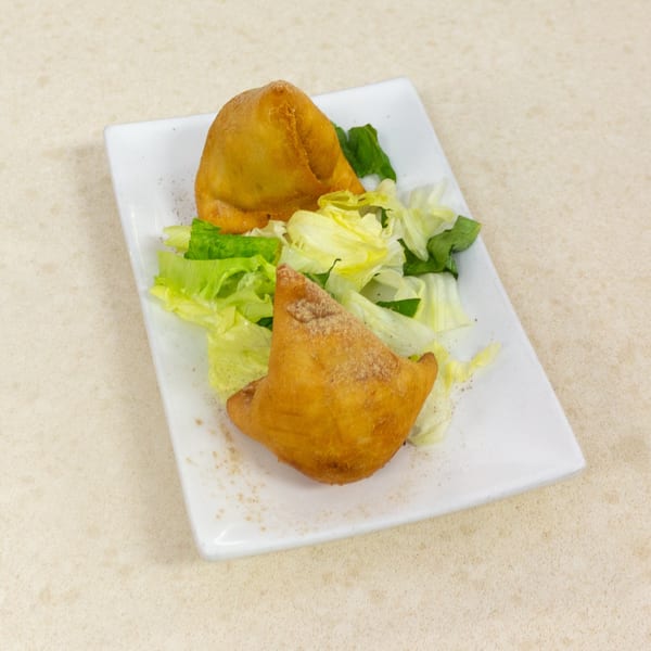 Two golden-brown samosas dusted with spices, served on a white rectangular plate with fresh lettuce.