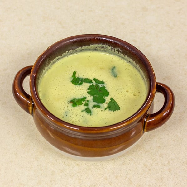 Creamy green soup in a brown ceramic bowl, garnished with fresh cilantro.