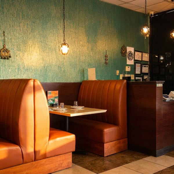 Empty restaurant interior with brown booths, teal walls, warm pendant lights, and a reception desk.