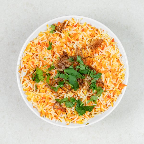 Overhead view of a white bowl filled with colorful biryani rice, garnished with fried onions and cilantro.