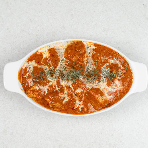 Overhead view of a white oval dish filled with orange chicken curry, drizzled with cream and herbs.