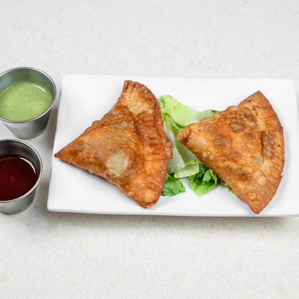 Two golden-brown fried samosas on a white plate with lettuce, served with green and red dipping sauces.