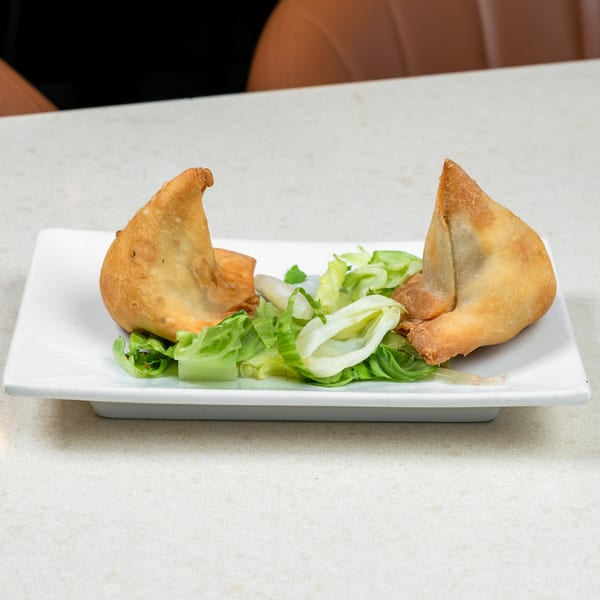 Two golden-brown samosas with a side of fresh green lettuce on a white rectangular plate.