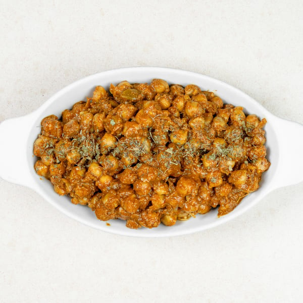 A white oval dish filled with chana masala, a chickpea curry, garnished with dried herbs.