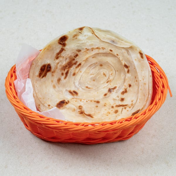 A round, flaky paratha bread with browned spots, served in an orange basket lined with white paper.