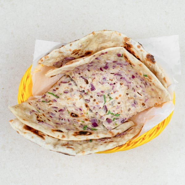 A yellow basket filled with onion naan bread, garnished with red onions and cilantro.