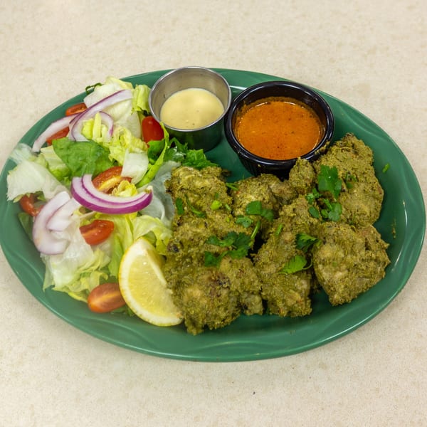 Green plate with chicken tikka, side salad, lemon wedge, and two dipping sauces.