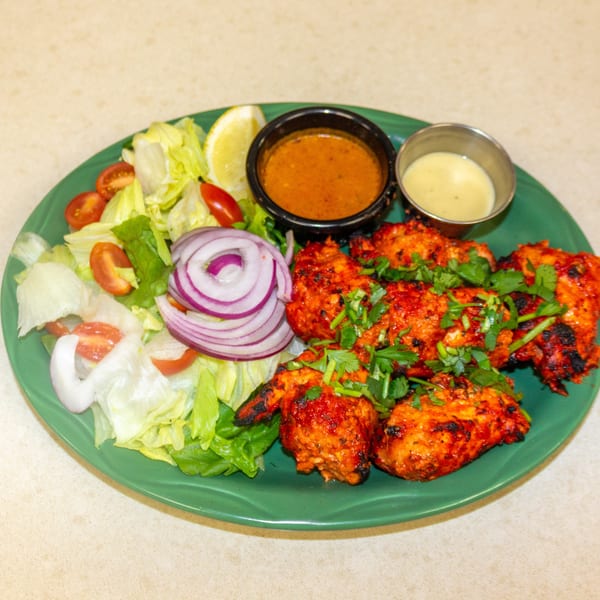 Tandoori chicken with cilantro, a side salad with red onions, and two dipping sauces on a green plate.