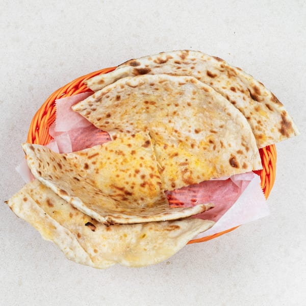Basket of warm, golden-brown flatbreads with charred spots, lined with pink and white paper.
