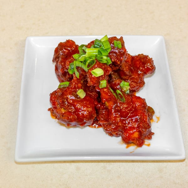 Spicy red chicken wings, garnished with chopped green onions, on a white rectangular plate.