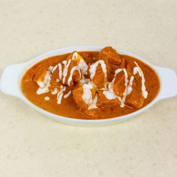 A white oval dish filled with chicken tikka masala, drizzled with white cream, on a light countertop.