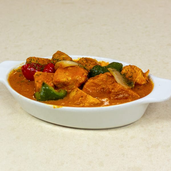 A white oval dish filled with chicken curry, bell peppers, and onions in a rich orange sauce.