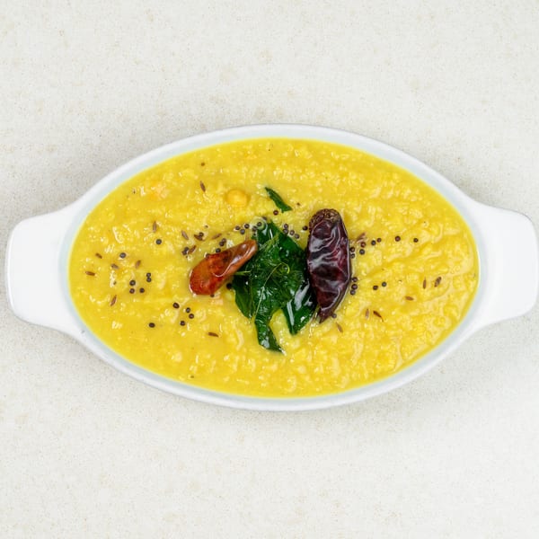 Yellow lentil dal in a white oval dish, garnished with curry leaves, red chilies, and spices.