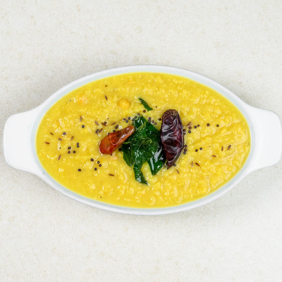 Yellow lentil dal in a white oval dish, garnished with red chilies, curry leaves, and spices.