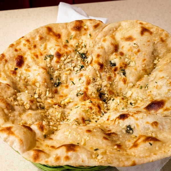 Round golden garlic naan bread with chopped garlic and green herbs on a table.