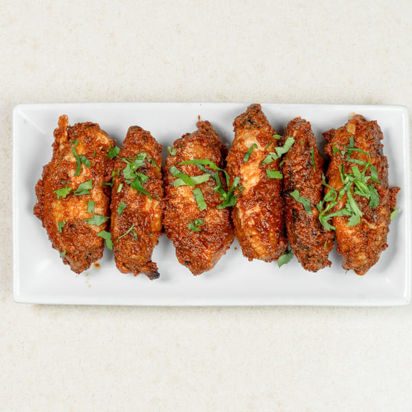 Six chicken wings coated in a rich red sauce and garnished with fresh green herbs on a white platter.