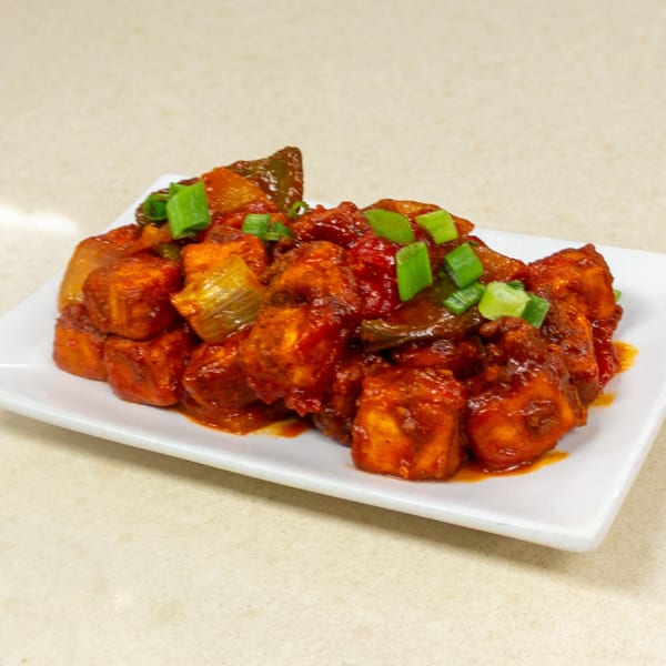 Spicy paneer chili with bell peppers and onions, garnished with green onions on a white plate.