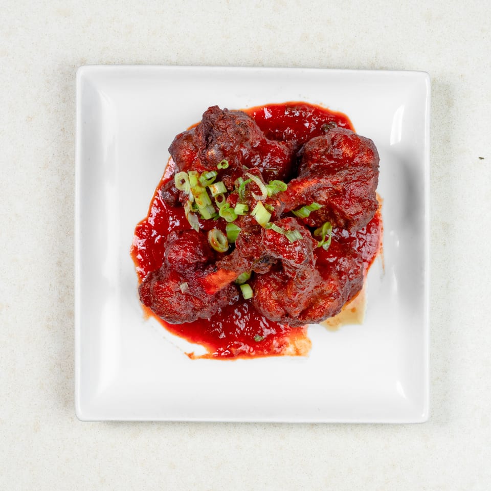 Top-down view of five chicken wings covered in red sauce and green onions on a white plate.