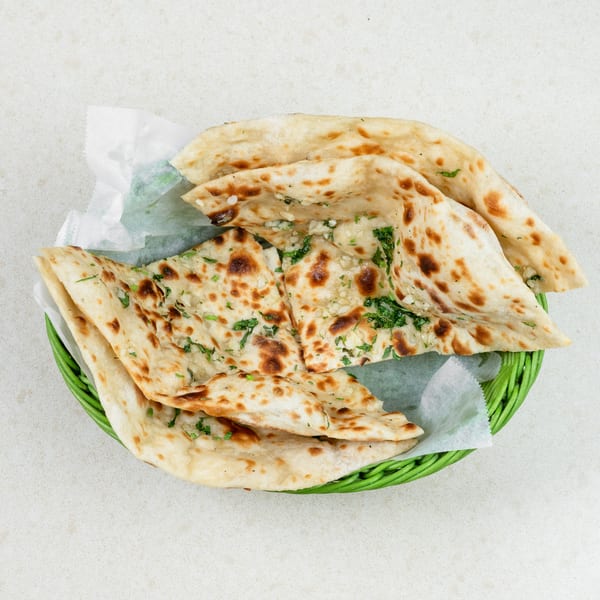 A green basket filled with several pieces of garlic naan bread, garnished with fresh cilantro.