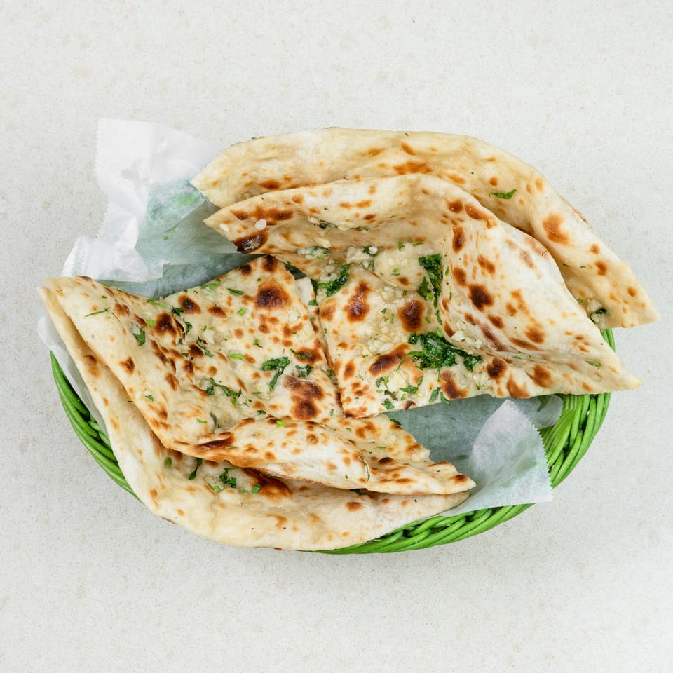 A green basket filled with several pieces of garlic naan bread, garnished with fresh cilantro.