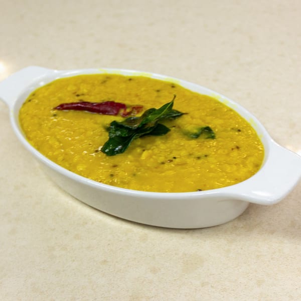 A white oval dish filled with yellow lentil dal, garnished with a red chili and green curry leaves.