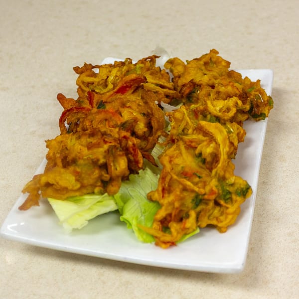 Golden-brown pakoras, a fried Indian snack, served on a white rectangular plate with lettuce.